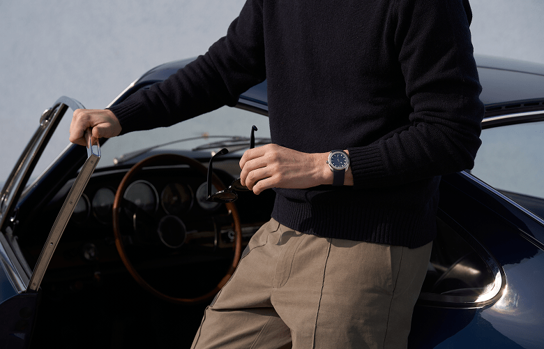 Image of a man wearing an luxury watch, leaning up against a car.